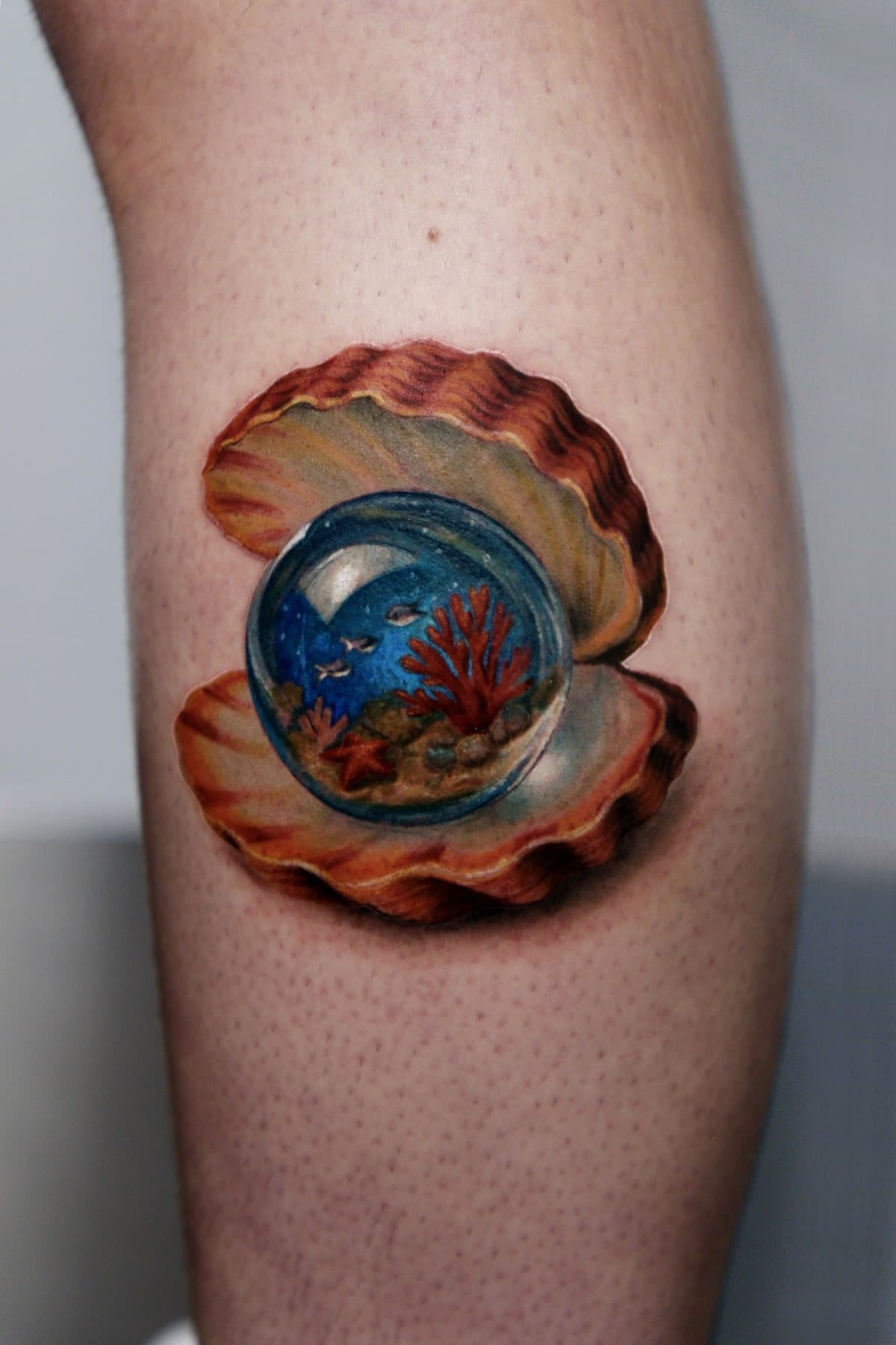 İçinde küçük bir mercan resifi olan cam küreyi taşıyan açık deniz kabuğu renkli realizm dövmesi, Global Tattoo Magazine'de yer alan işlerden biri